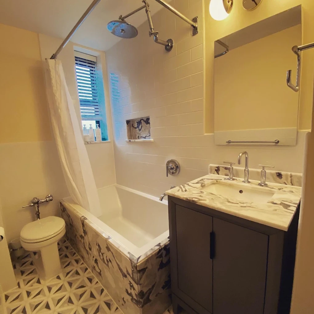 Bathroom with a veined stone vanity top and bathtub surround, rain shower, and patterned floor